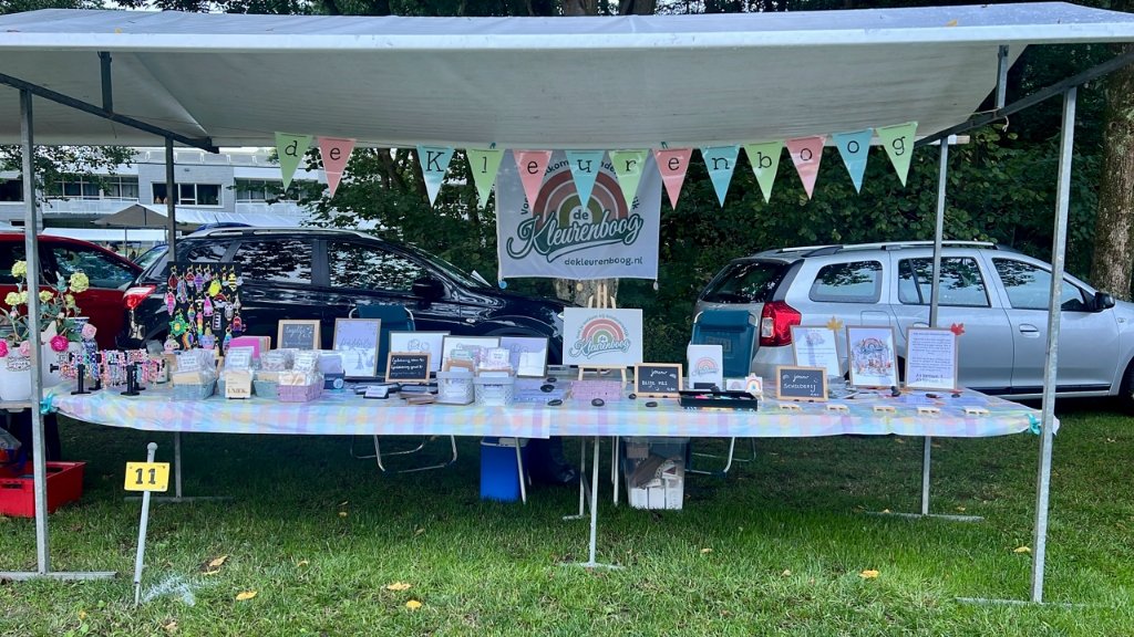 Overzicht van de vrolijk versierde marktkraam van Kinderpraktijk De Kleurenboog op de zomermarkt in Wapenveld